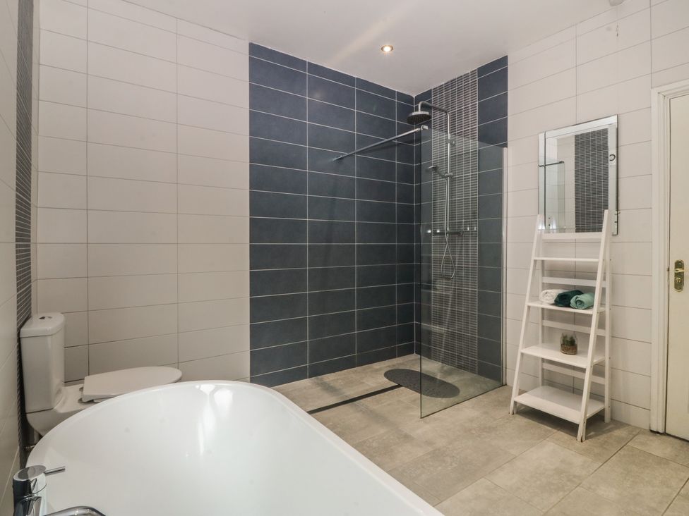 A bathroom with a bathtub, shower, and shelving unit at Gwylan Uchaf Y Felinheli