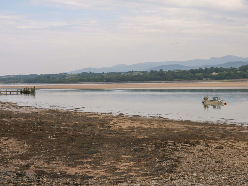 A view of a boat on the water near a pier with mountains in the background at Menai Cottage in Brynsiencyn