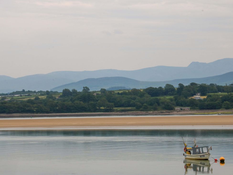 A boat on the water with mountains in the background at Menai Cottage in Brynsiencyn