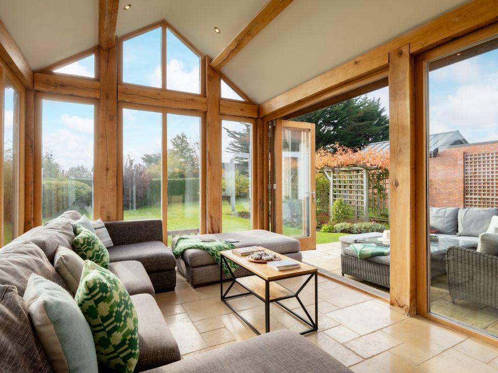 A conservatory with a sofa and coffee table overlooking a garden at Summerfield in Deganwy