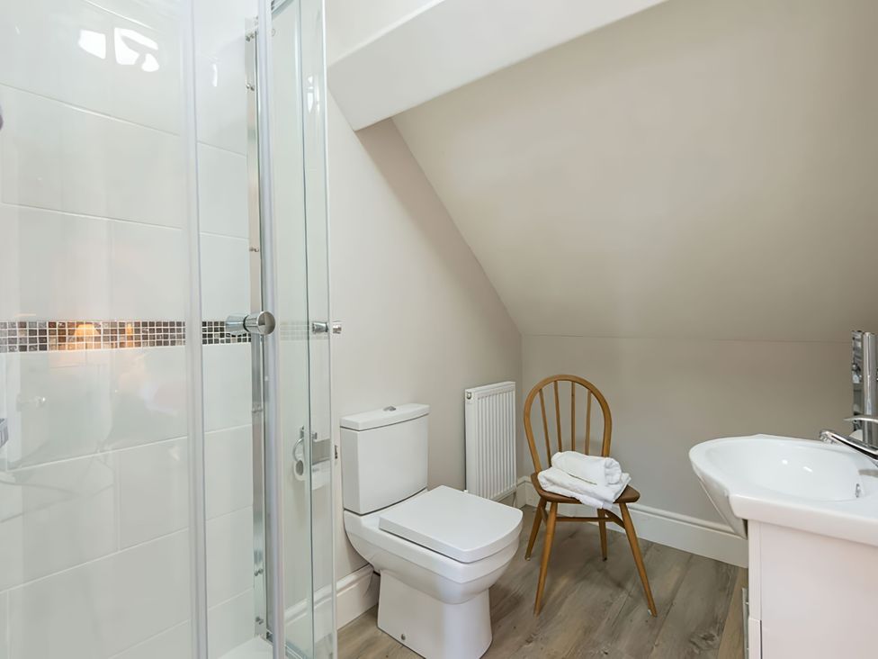 A bathroom with a shower, toilet, sink, and a chair at West View in Rhosneigr