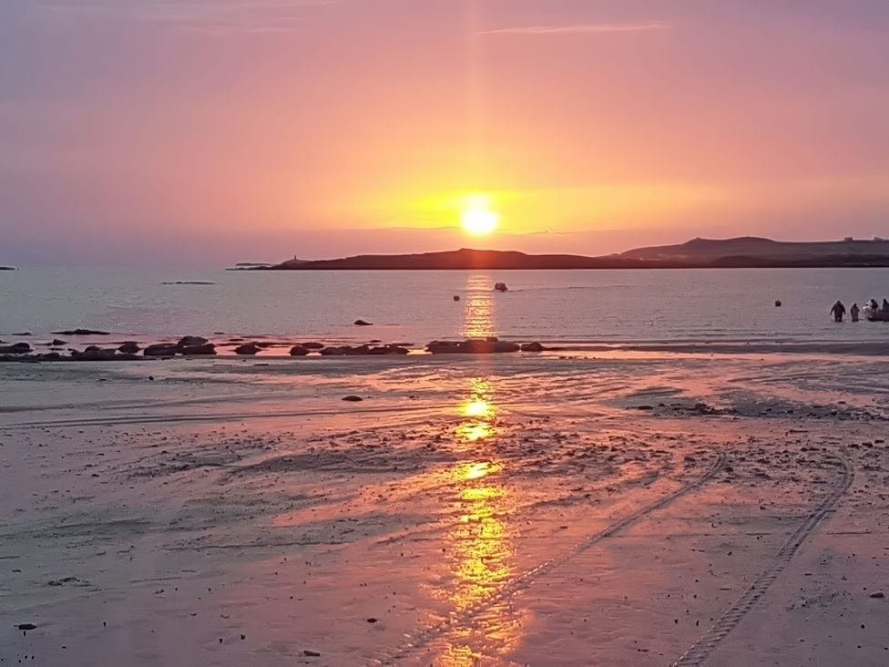 A sunset over the ocean with people standing on the sand at West View in Rhosneigr