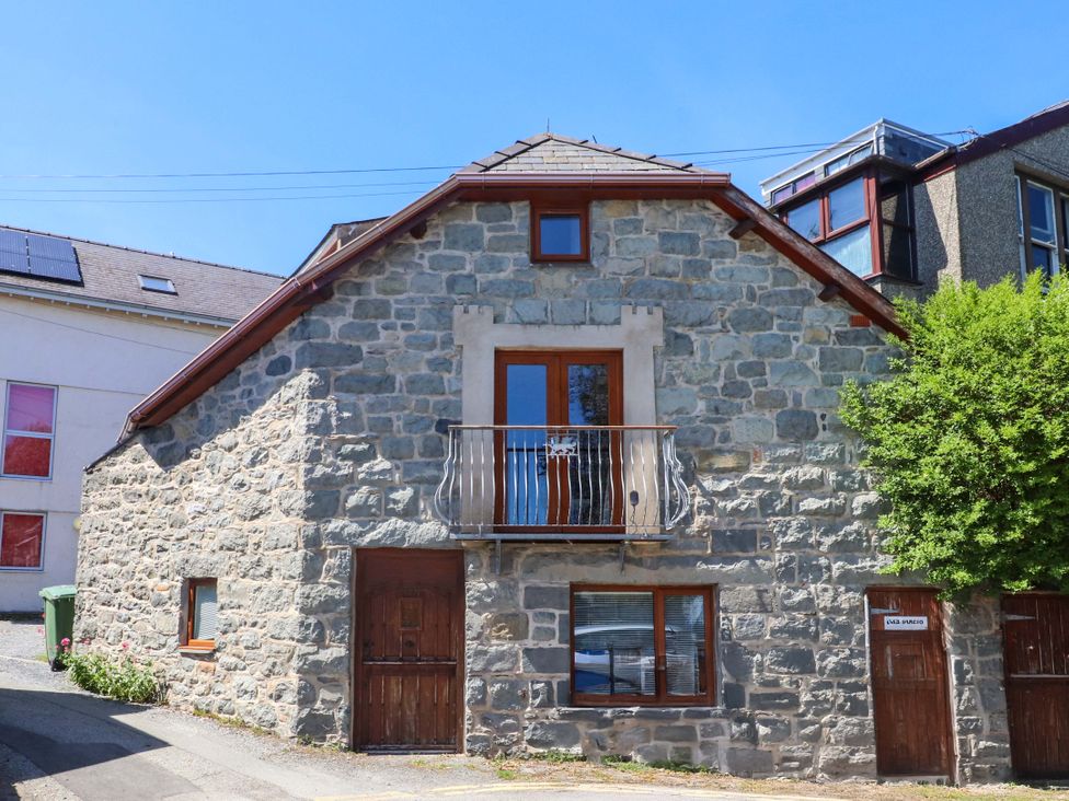 A stone house with wooden doors and windows and a small balcony at Y Stabl in Criccieth