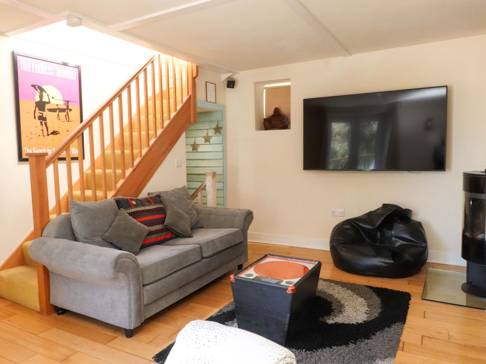 A living room with a grey sofa and cushions a black beanbag a large wall mounted TV and wooden stairs at Y Stabl in Criccieth