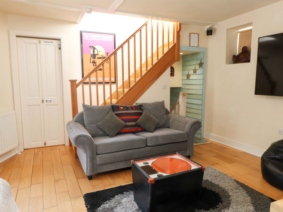 A living room with a gray sofa a black and orange coffee table and wooden stairs at Y Stabl in Criccieth