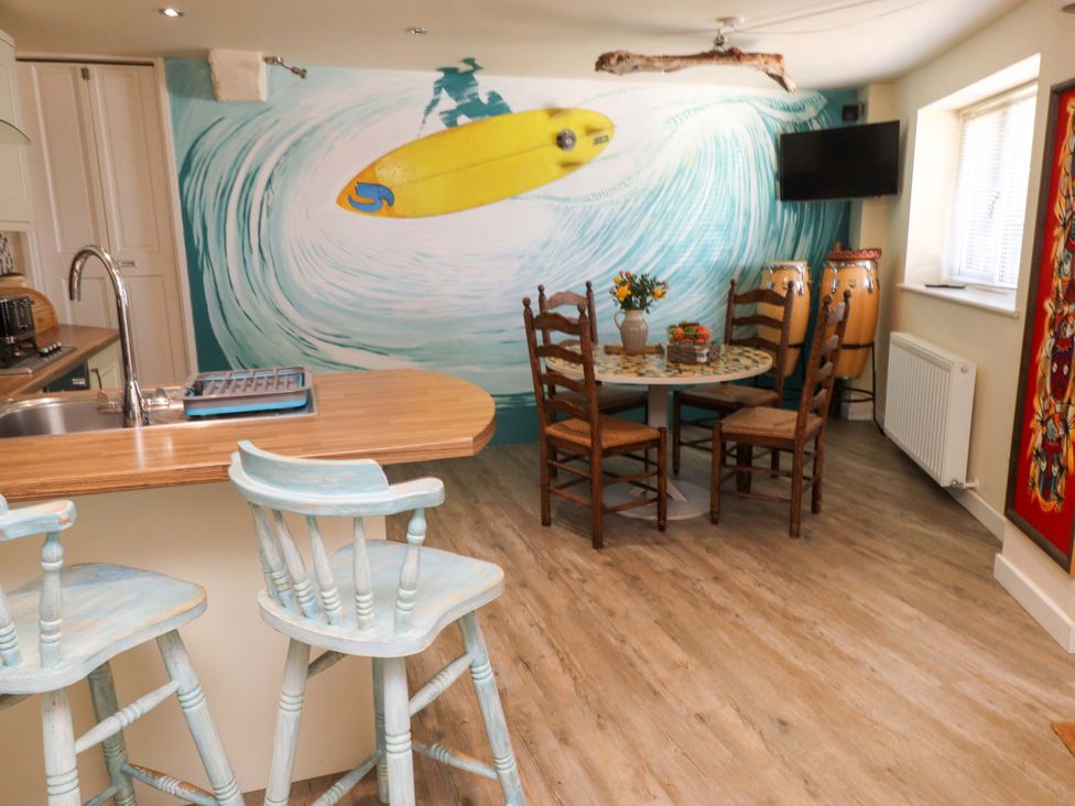 A kitchen and dining area with a surfboard wall mural and wooden chairs at Y Stabl in Criccieth