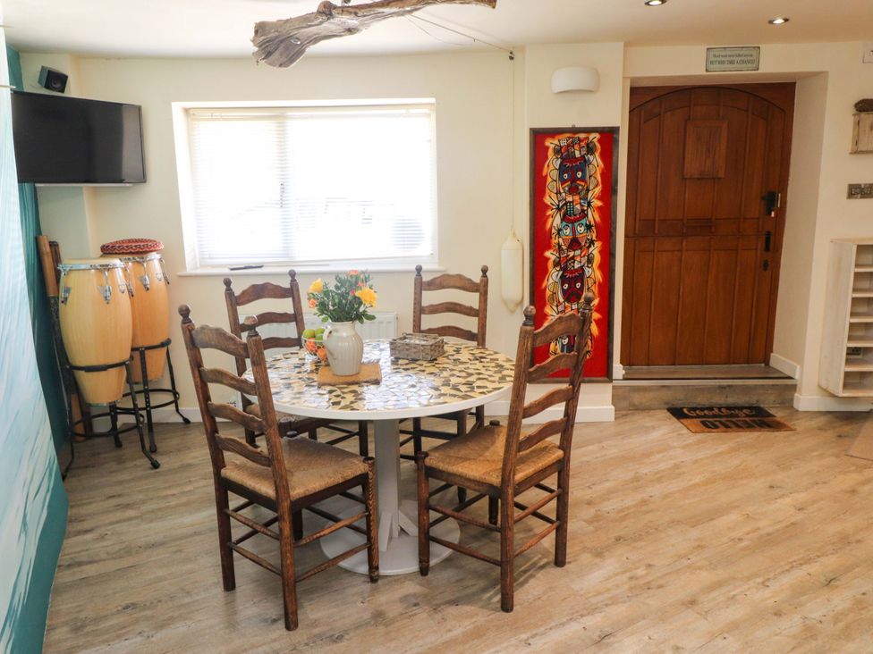 A dining area with a round table and four wooden chairs near a window and a wooden door at Y Stabl in Criccieth