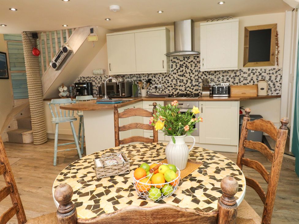 A kitchen and dining area with mosaic table a fruit bowl and flowers at Y Stabl in Criccieth