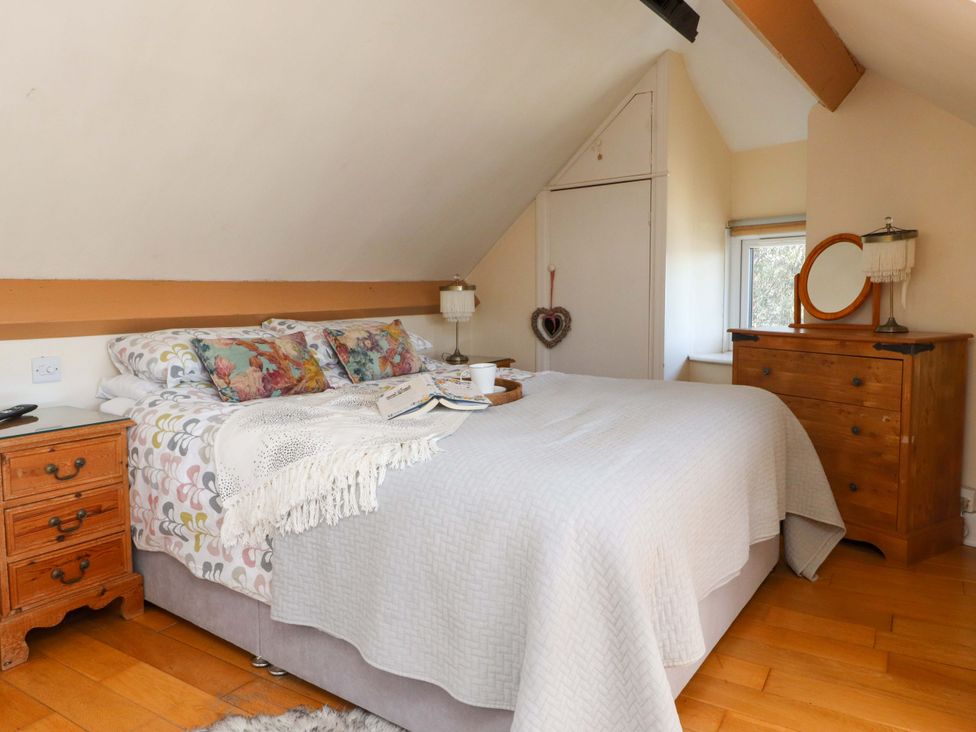A bedroom with a bed with patterned pillows a wooden nightstand and a wooden dresser with a mirror at Y Stabl in Criccieth