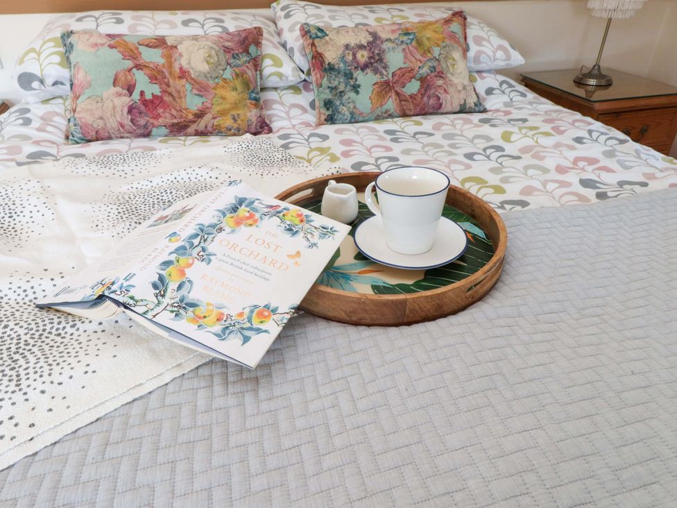 A bed with floral pillows and patterned bedding with a book and a tray holding a cup and a small pitcher on it at Y Stabl in Criccieth