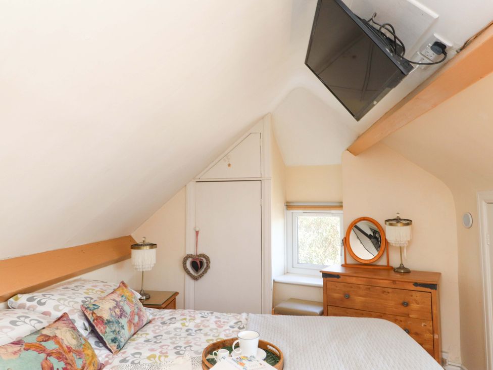 A bedroom with a bed a wooden dresser a wall-mounted TV and a small window at Y Stabl in Criccieth