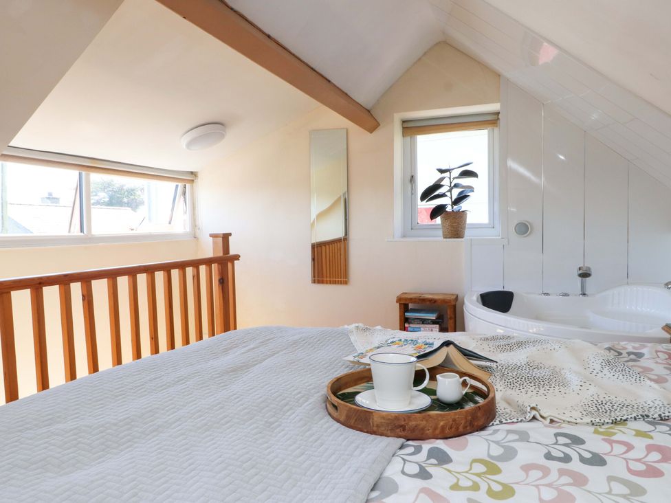 A bedroom with a bed a wooden railing a window and a bathtub at Y Stabl in Criccieth