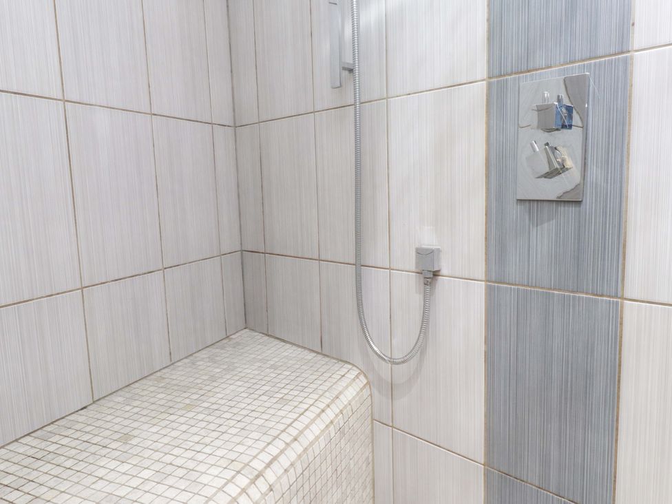A tiled shower area with a built-in bench and a shower control at Y Stabl in Criccieth