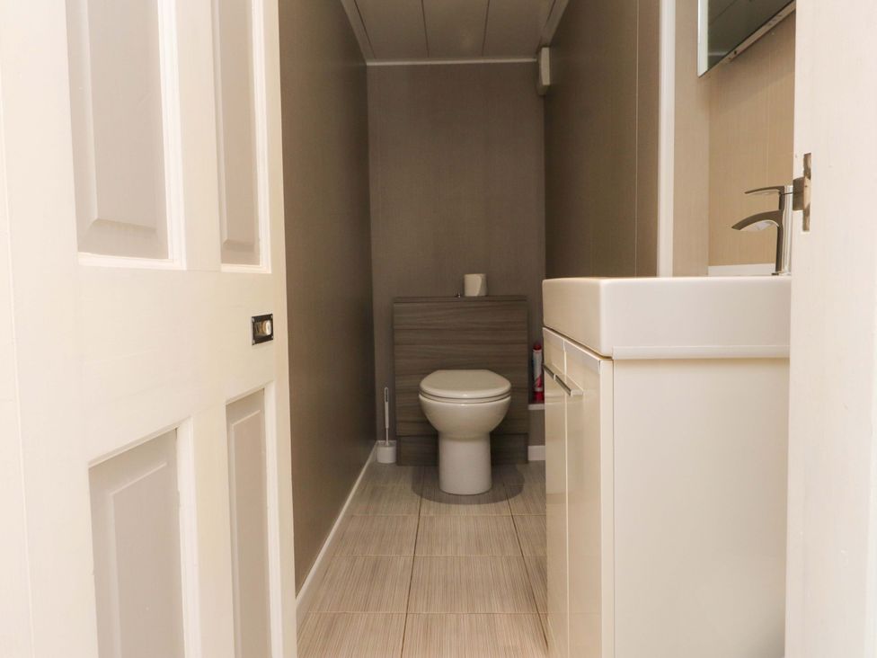 A bathroom with a toilet a toilet brush a sink with a faucet and a cabinet at Y Stabl in Criccieth