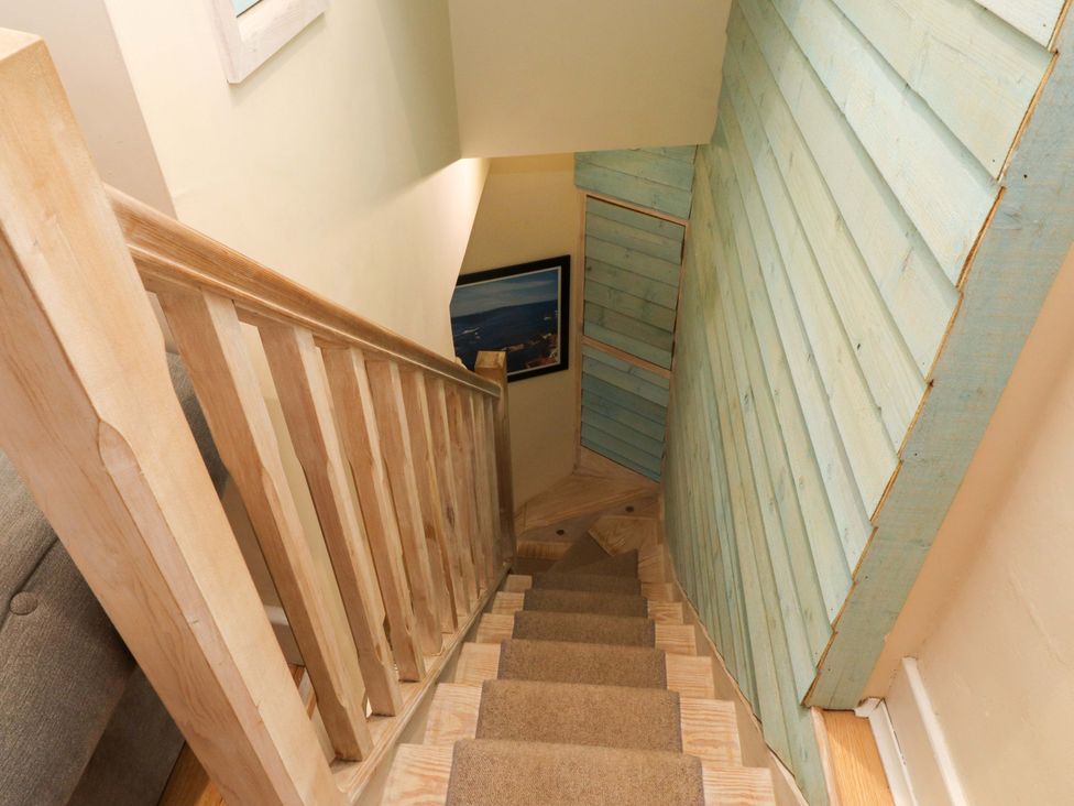 A staircase with wooden railing carpeted steps and blue wooden paneling on the wall at Y Stabl in Criccieth