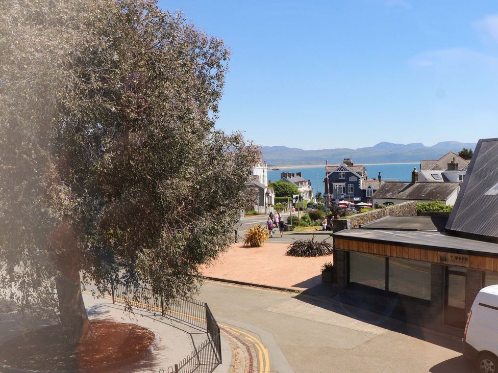 A street view with a large tree on the left a building on the right and the sea with mountains in the background at Y Stabl in Criccieth
