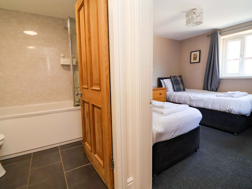 A bathroom with a bathtub and toilet adjoining a bedroom with two beds at Clwyd Cottage St Asaph