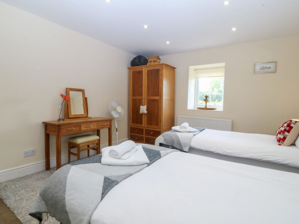 A bedroom with two beds and a wooden wardrobe at Llanallgo Church Rooms 