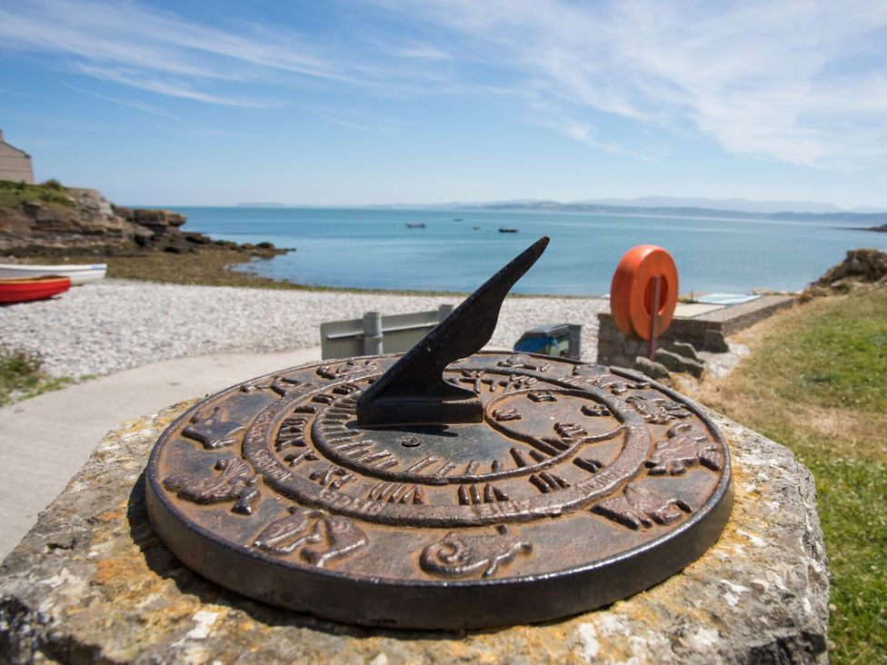 A sundial near the sea with rocks and boats at Llanallgo Church Rooms