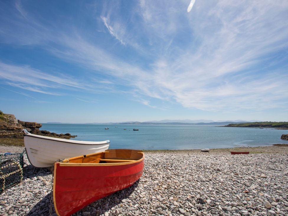 Two boats on a pebble beach with water in the background at Llanallgo Church Rooms