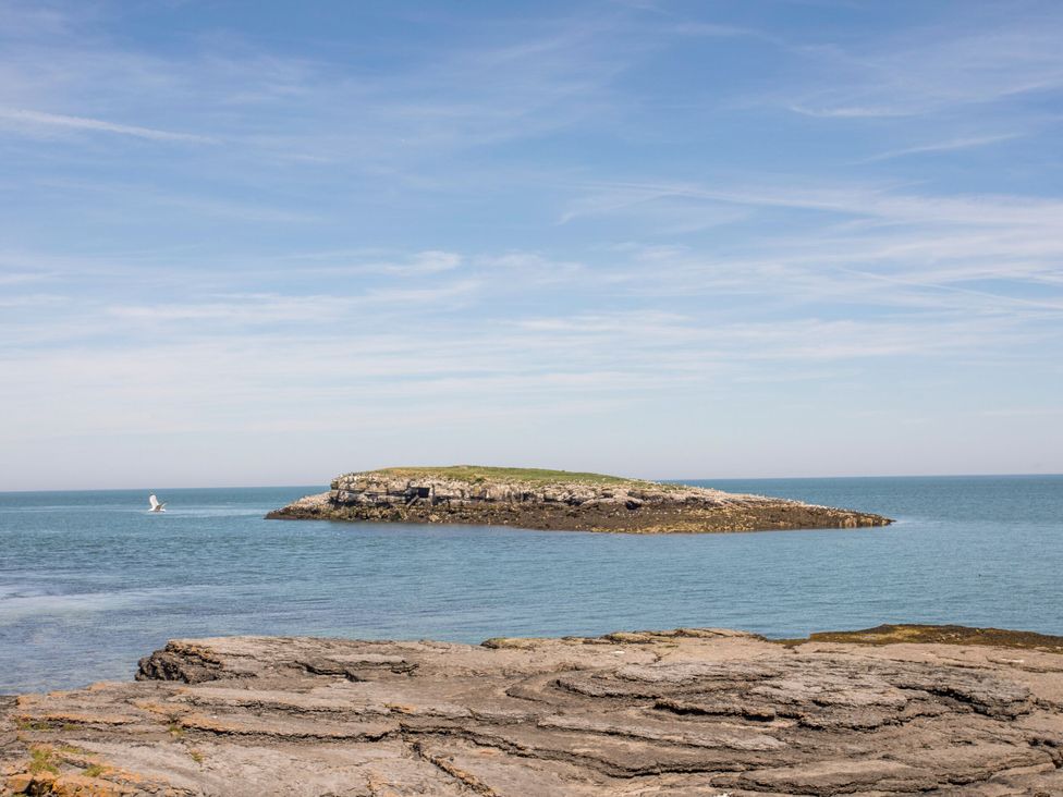 An island visible from a rocky shore with a boat in the sea at Llanallgo Church Rooms