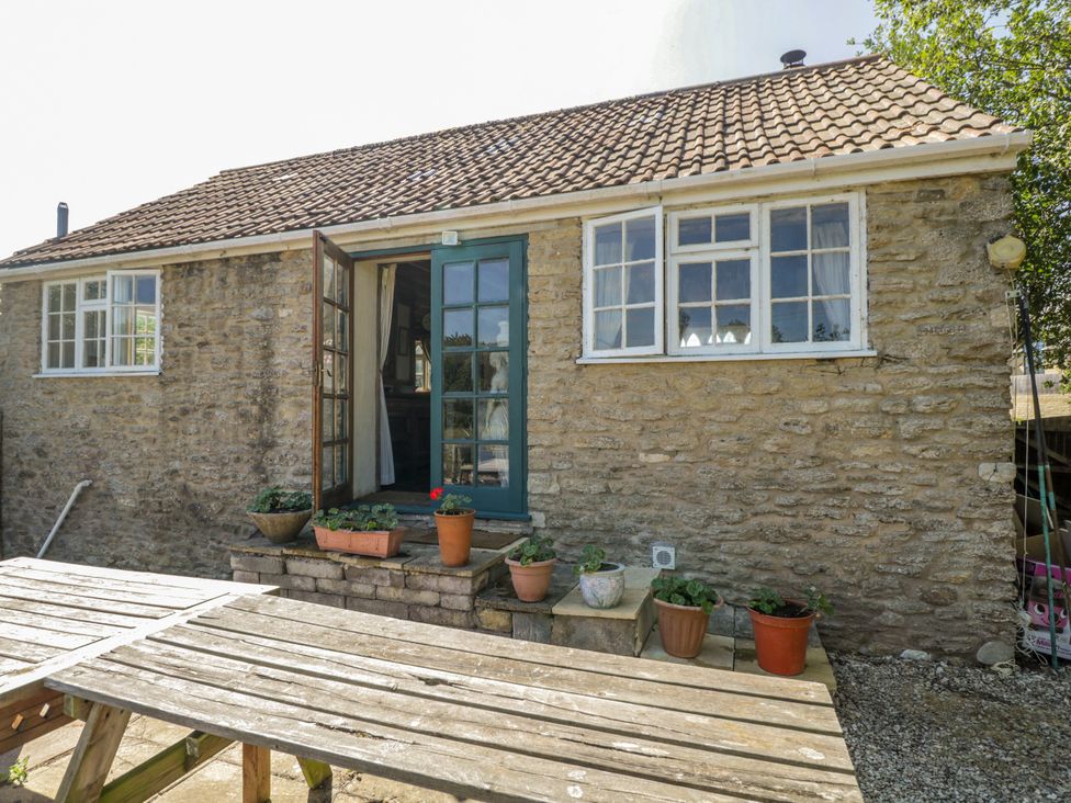 An outdoor area with a stone house and a wooden table at Ivy Cottage Woolverton near Beckington