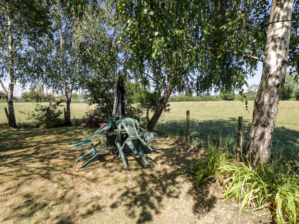 A garden with stacked chairs and table under an umbrella at Ivy Cottage Woolverton near Beckington