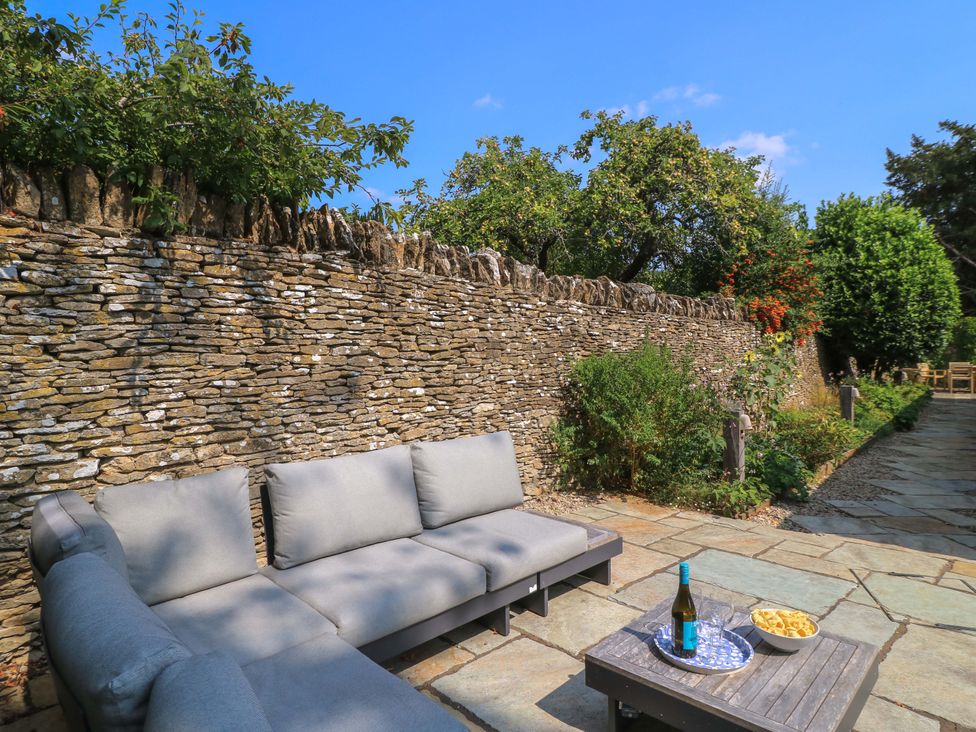 An outdoor seating area with a sofa and a stone wall at Easter Cottage in Burford