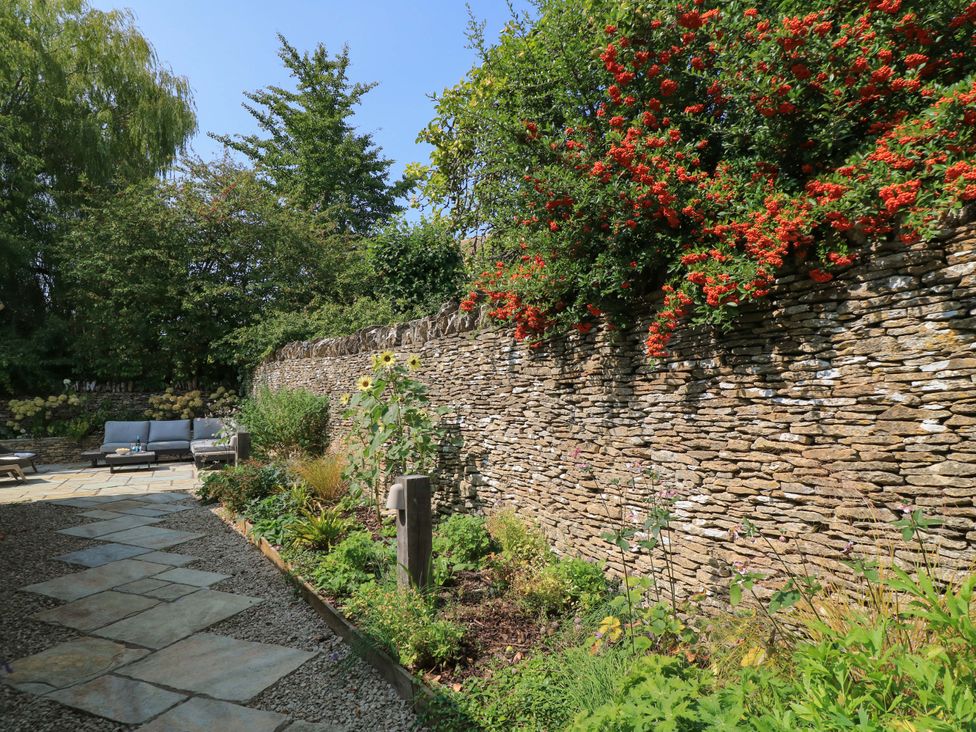 A garden with a stone wall and seating area at Easter Cottage in Burford
