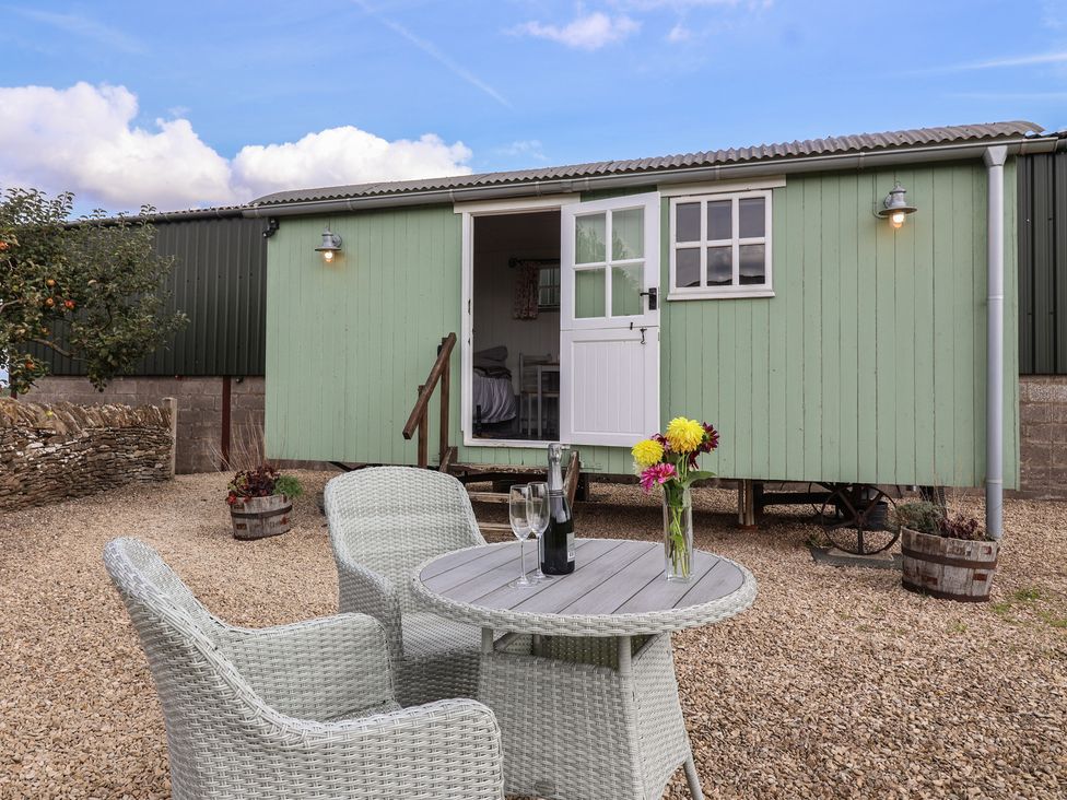 An outdoor setting with a green hut, table and chairs at The Shepherds Hut in Chippenham