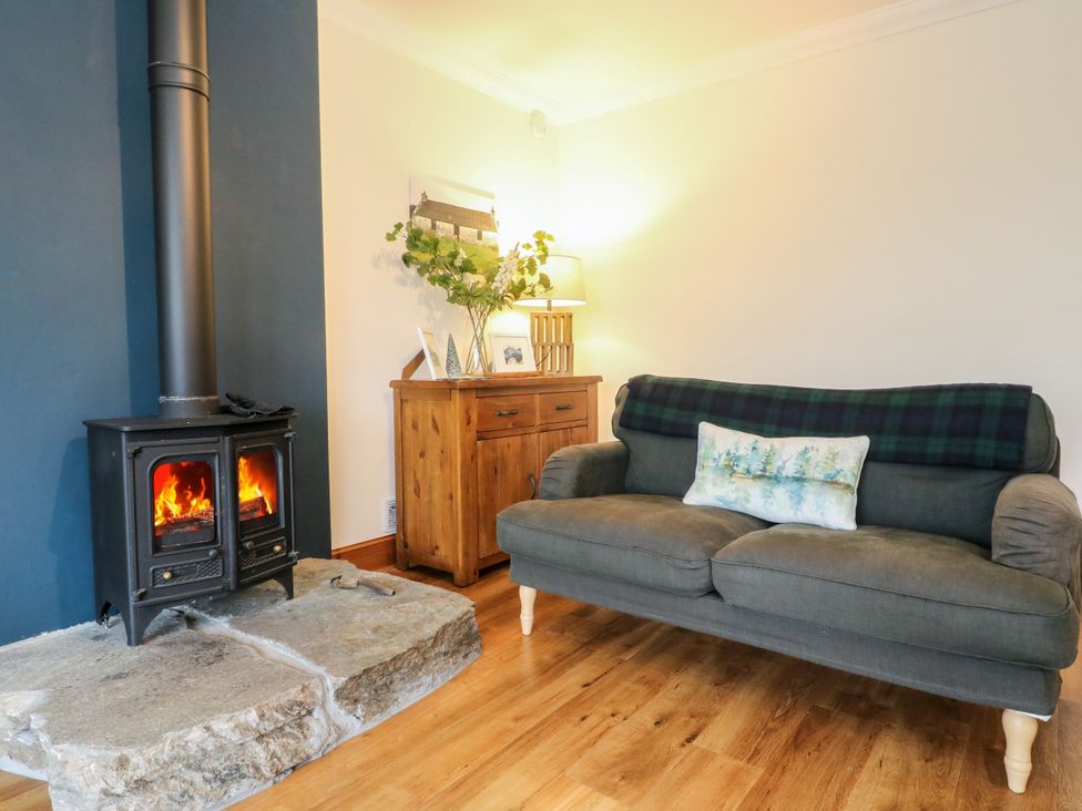 A living room with a wood stove and sofa at Thistle Do in Lochailort