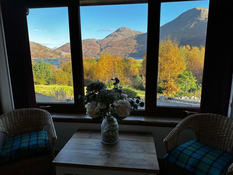 A living room with a table and flowers near windows overlooking mountains at Thistle Do in Lochailort