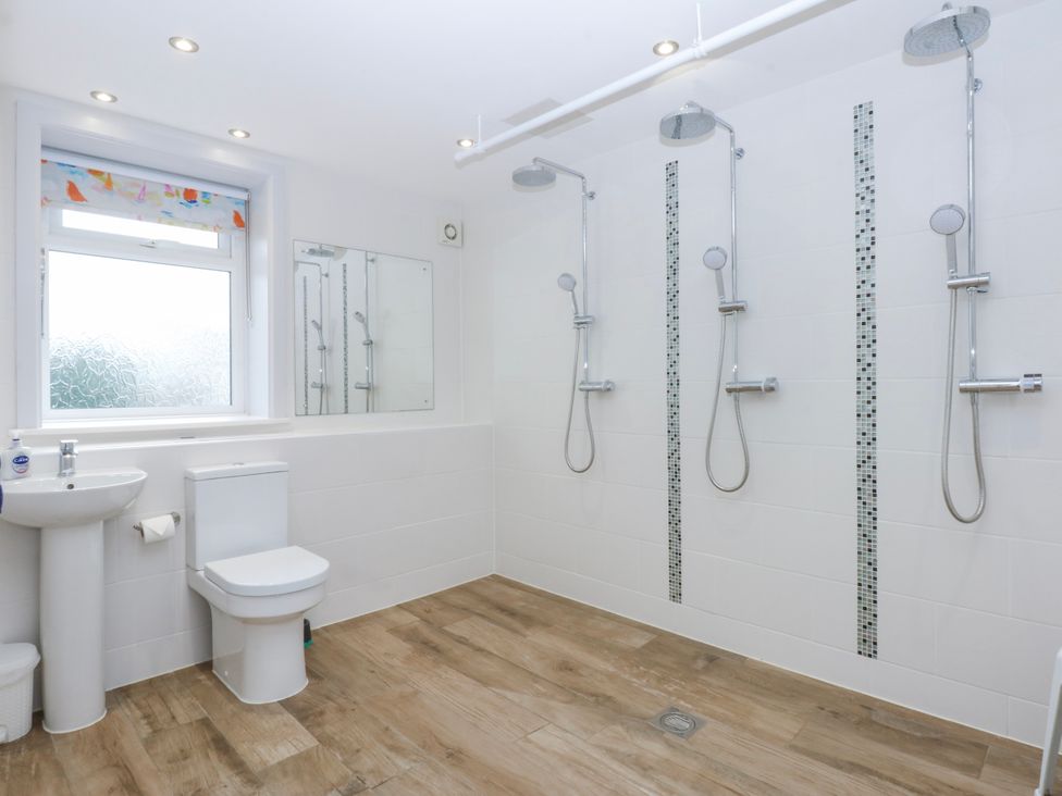 A bathroom with three showers, a toilet, sink, and window at Bwthyn Alberts in Trearddur Bay