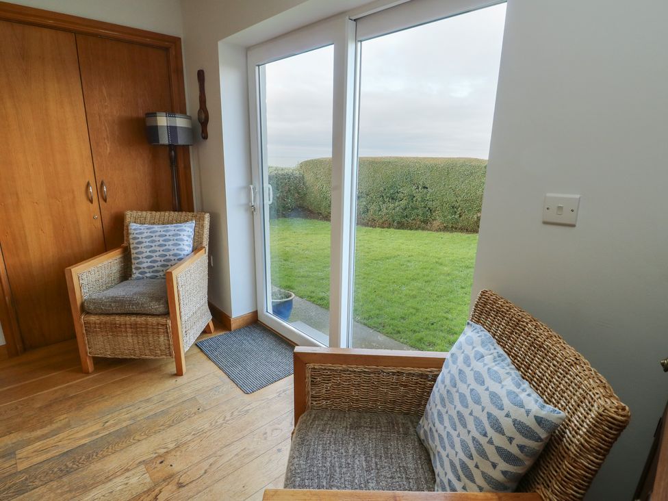 A sunroom with two armchairs and a sliding door at Yr Orsedd in Llanfaethlu