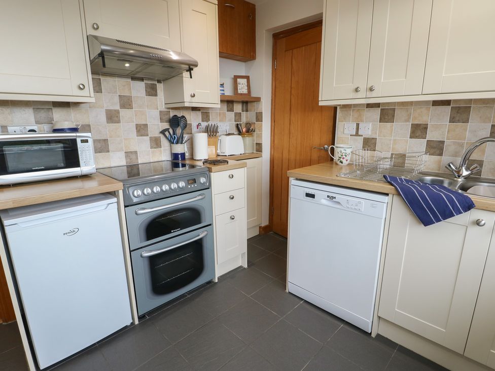 A kitchen featuring a sink, oven, microwave, and dishwasher at Yr Orsedd in Llanfaethlu