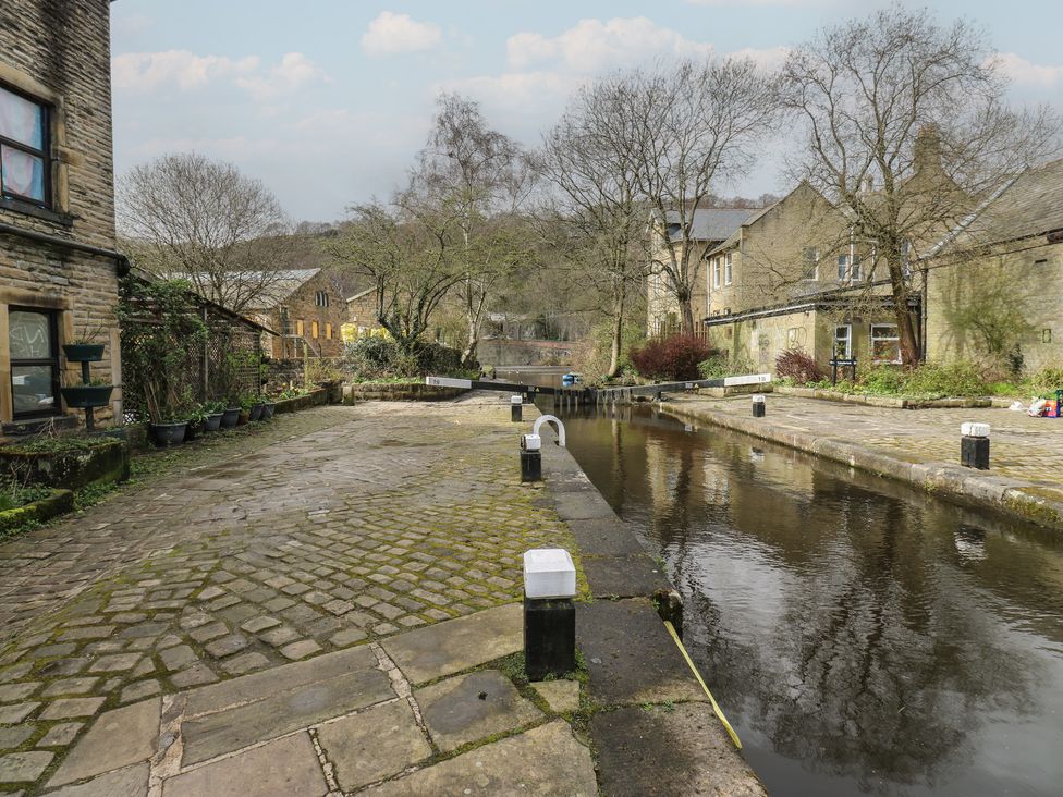 A canal with a pathway beside buildings and trees at Shoebroad Barn Todmorden