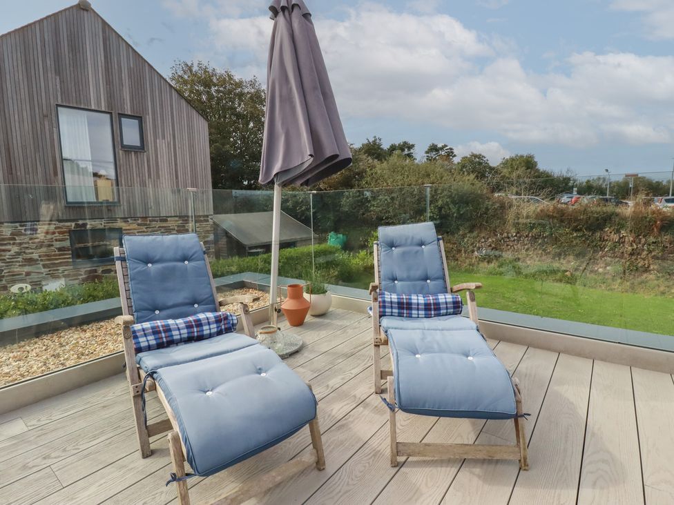 An outdoor patio with sun loungers and an umbrella at Idlewild, 2 Wheal Turnavore, St Agnes