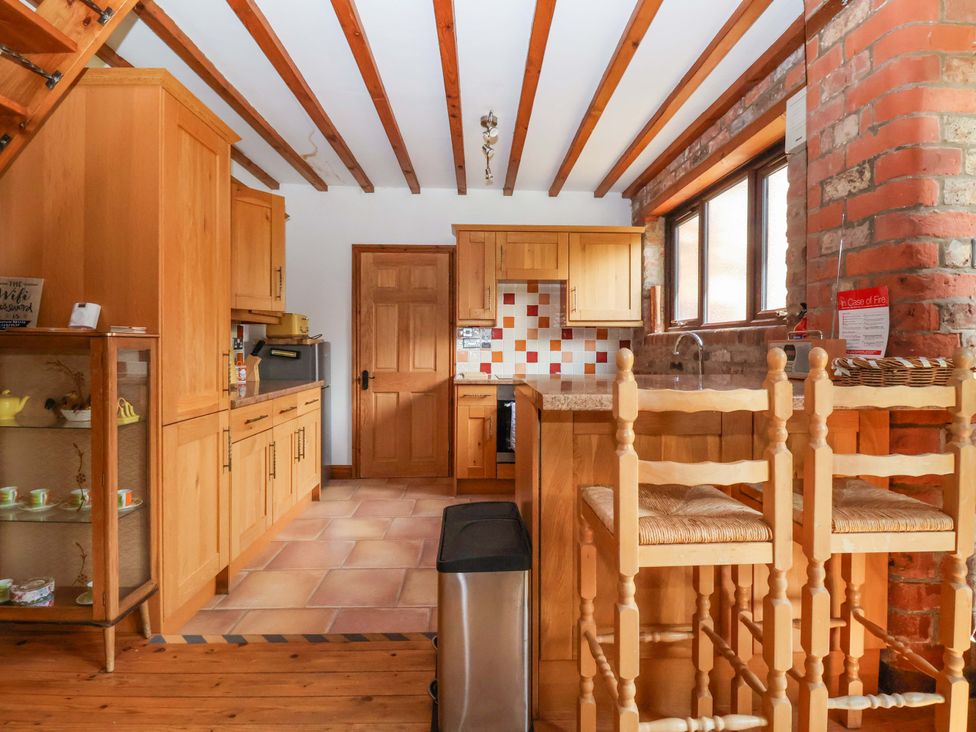 A kitchen with wooden cabinets and bar stools at The Stables (2 bed) in Driffield