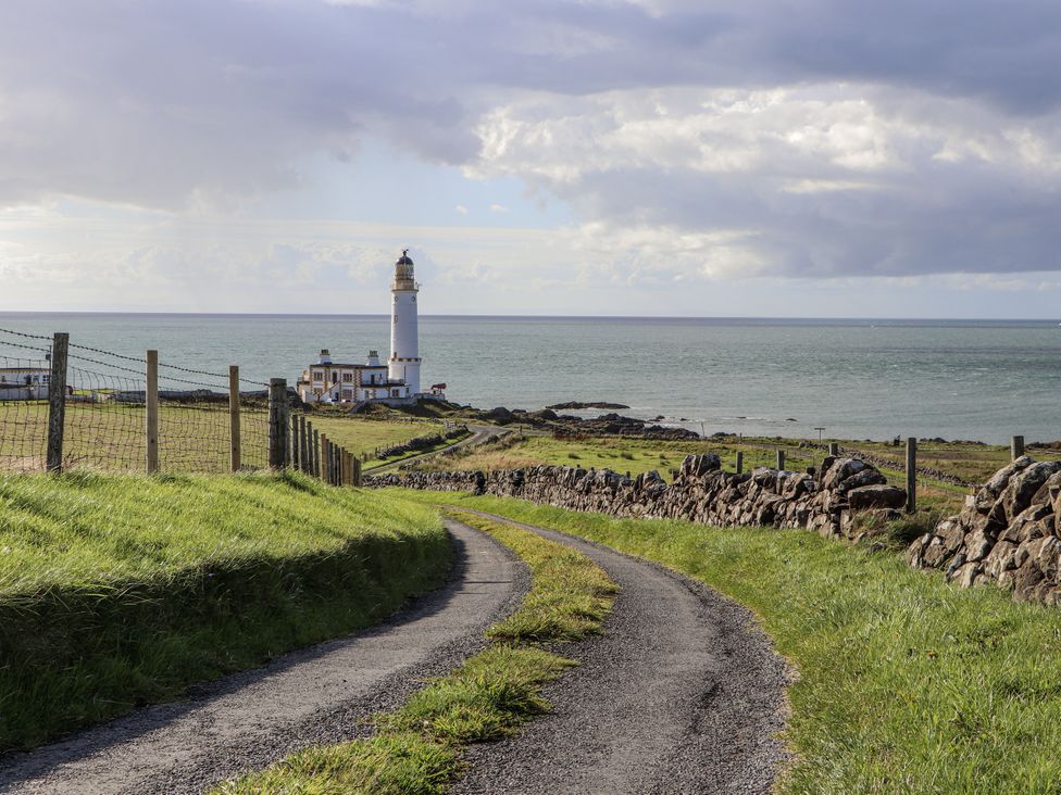 A lighthouse near the sea with a path leading to it at Corsewall Castle Farm Lodges in Kirkcolm