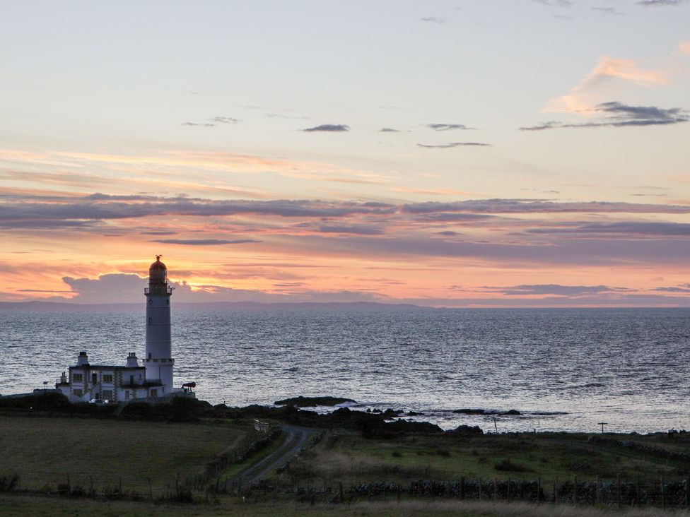 A lighthouse beside the ocean during sunset at Corsewall Castle Farm Lodges in Kirkcolm