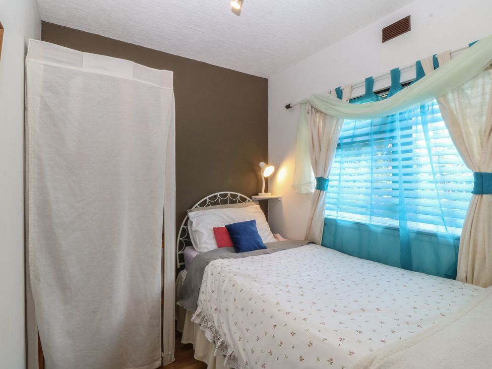 A bedroom with a bed, lamp, and window at Castell Chalet in Penrhos near Pwllheli