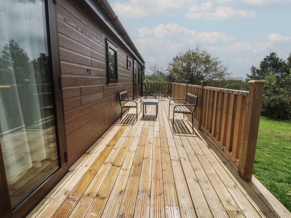 An outdoor wooden deck with chairs and a table at Castell Chalet Penrhos near Pwllheli