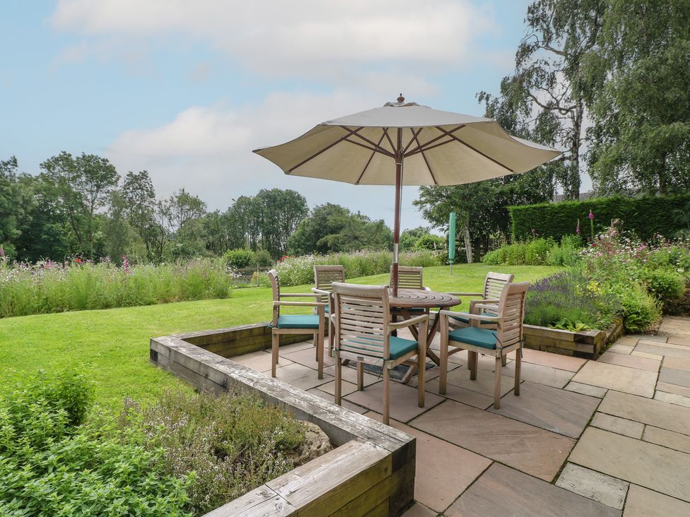 A patio with a table and chairs under an umbrella at Ivet Lowe Hopton near Wirksworth