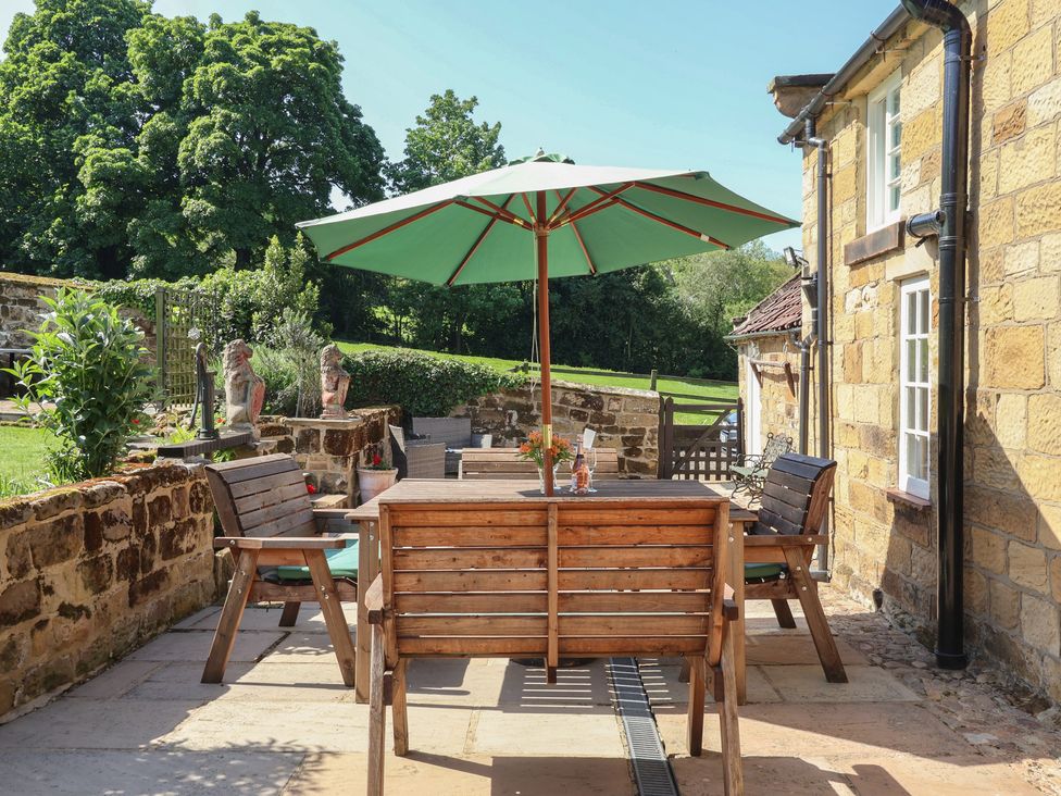 A garden with outdoor table and chairs under a parasol at Webstone House in Thimbleby near Osmotherley