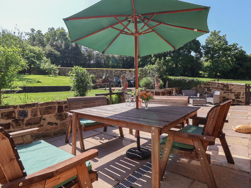 A garden with a wooden table and chairs under an umbrella at Webstone House Thimbleby near Osmotherley