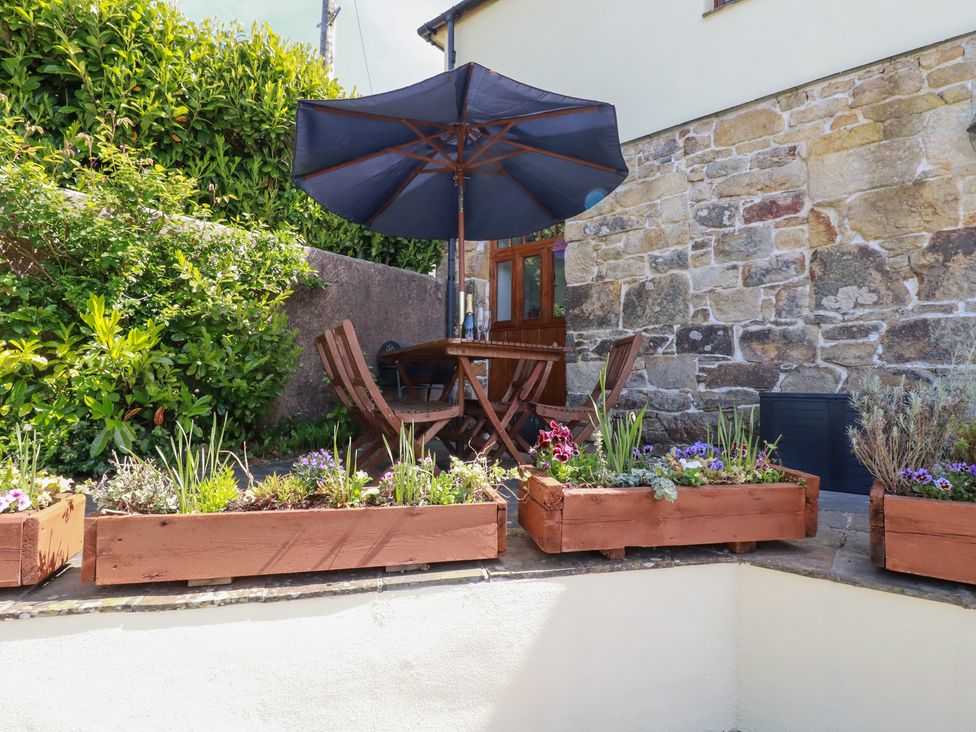 An outdoor patio with a wooden table and chairs under a large umbrella surrounded by flower boxes at The Hayloft in Sticker