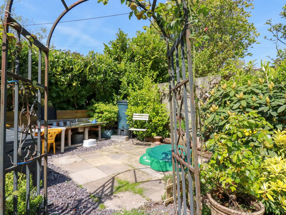 A garden with a metal archway stone patio green plants a green plastic turtle sandbox a white chair and outdoor sink at The Hayloft in Sticker