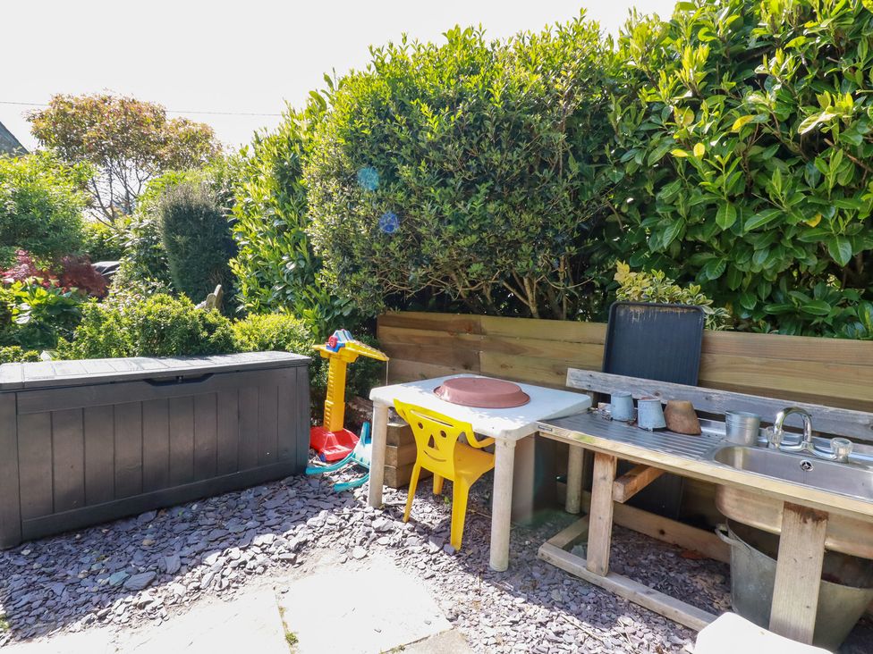 An outdoor area with a yellow child chair and table a black storage box a toy crane a wooden sink with metal pots and green bushes at The Hayloft in Sticker