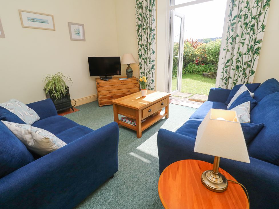 A living room with blue sofas a wooden coffee table and TV with doors leading to a garden at Old Chapel Cottage Trescowe near Praa Sands
