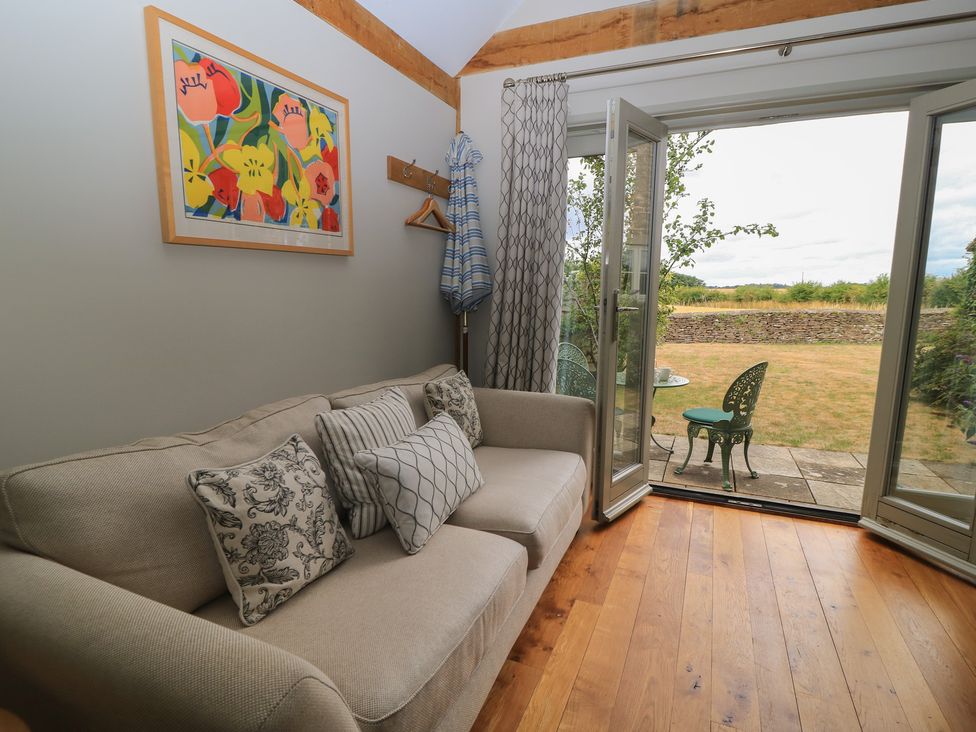 A living room with a sofa and open door leading to outdoor seating at The Lodge at Mortons in Hankerton
